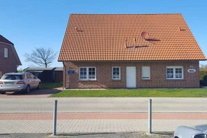 Ein eingeschossiges Backsteingebäude mit einem Ziegeldach, einem kleinen Vorgarten und einem geparkten Auto.
