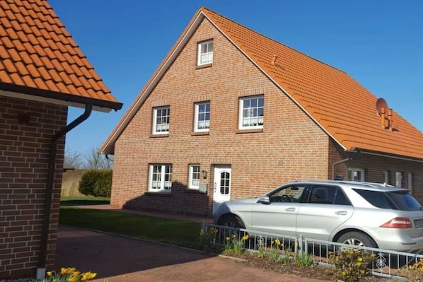 Ein zweistöckiges Backsteinhäuschen mit geneigtem Dach, einem Auto auf der Auffahrt und einem kleinen Garten mit gelben Blumen.