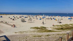 A beach with numerous tents and beach chairs, a lifeguard stand, and a clear sky. - Holiday home with 3 bedrooms (Dornumersiel)