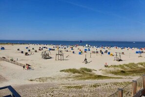Ein Strand mit vielen Zelten und Liegestühlen, einem Rettungsschwimmerstand und blauem Himmel.