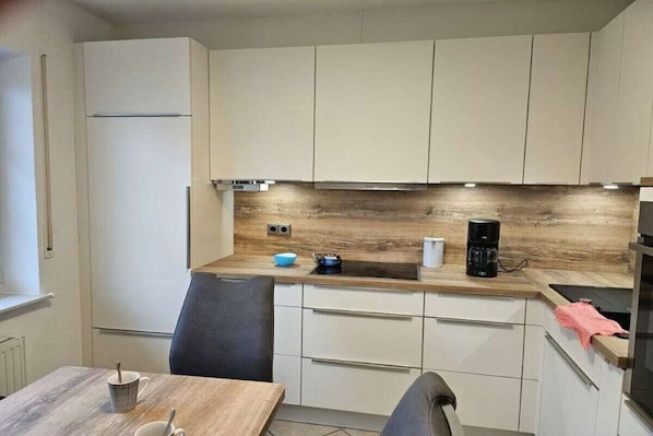 Een moderne keuken met witte kastjes, een houten aanrechtblad en een koffiezetapparaat.