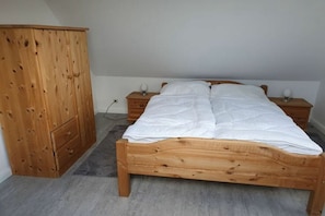 Een slaapkamer met een houten bed, een kledingkast van hout en nachtkastjes met lampen.