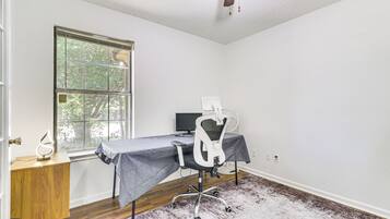 Una habitación con escritorio de madera, una silla, computadora y ventana con vista a árboles.