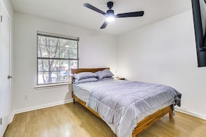 Ein Schlafzimmer mit einem Bett, einem Fenster, einem Deckenventilator und einem Nachttisch.