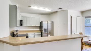Una cocina con armarios blancos, un refrigerador de acero inoxidable y una encimera de granito.