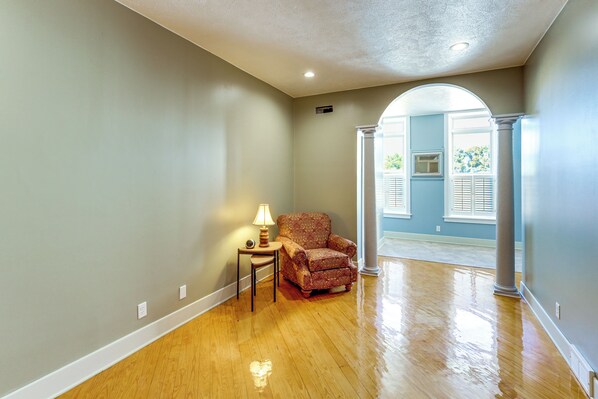 A room with hardwood flooring, a patterned armchair, a small table with a lamp, and a doorway leading to another room.