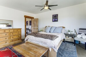 Une chambre à coucher comprenant un lit, une commode en bois, un ventilateur de plafond et une table de chevet avec une lampe.