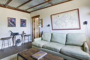 Une pièce avec un canapé vert, une table basse en bois, une carte accrochée au mur et un coin bar avec des tabourets.
