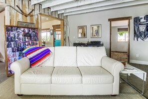 A room with a white leather sofa, a colorful artwork on the wall, and a door leading to another room. - Pool, Spa & Stargazing! Private Desert Retreat (Twentynine Palms)