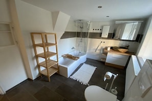 Ein modernes Badezimmer mit Badewanne, Dusche und Toilette. Ein Holzboden und ein weißer Teppich liegen auf dem Boden.