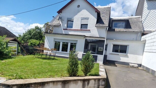 Uma casa de dois andares com um jardim da frente, um pequeno jardim e uma entrada para carros.