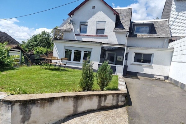 Ein zweistöckiges Haus mit Vordergarten, kleinem Garten und Auffahrt.