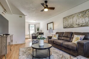 A living room with a brown leather sofa, a round coffee table, a patterned armchair, and a painting on the wall.