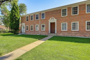 A two-story brick building with a central entrance, a covered porch, and a well-maintained lawn.
