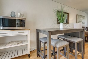 A modern kitchen with a microwave, a white cabinet, and a bar stool arrangement.