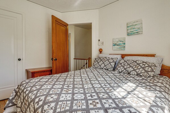 A bedroom with a large bed, a wooden door, a nightstand, and a painting on the wall.
