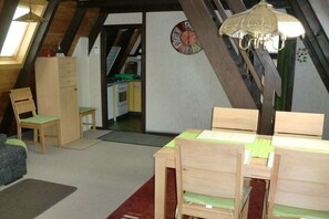 Une chambre à coucher aménagée dans un espace mansardé avec un plafond en pente, une table à manger en bois, une chaise, un petit meuble et une horloge murale.