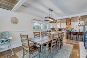 A spacious kitchen with a wooden dining table, bar stools, and a hanging light fixture.