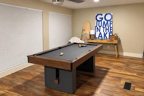 A pool table in a room with wooden flooring, a wall with a motivational sign, and a small table with a lamp and a wooden object. - Boat Dock & Game Room! Lake Hamilton Home (Hot Springs)