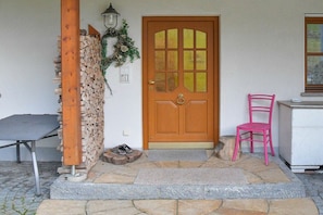 A wooden door with a glass panel, a stone step leading to the entrance, a metal bench, and a pink chair. - Holiday apartment with 1 bedroom (Salzweg)