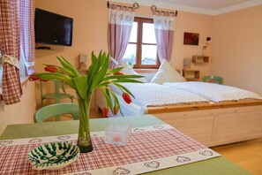 A bedroom with a bed, a television mounted on the wall, a window with curtains, and a table with a vase of flowers. - Holiday apartment with 1 bedroom (Salzweg)