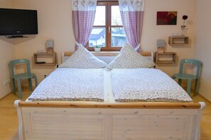 A bedroom with a double bed, two bedside tables, a television, a window with curtains, and a small potted plant. - Holiday apartment with 1 bedroom (Salzweg)