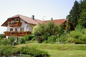 A two-story house with a red-tiled roof, a balcony with flower boxes, and a garden with various plants. - Holiday apartment with 1 bedroom (Salzweg)