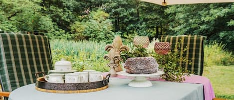 Un área de comedor al aire libre con una mesa dispuesta para servicio de té, rodeada de abundante follaje.