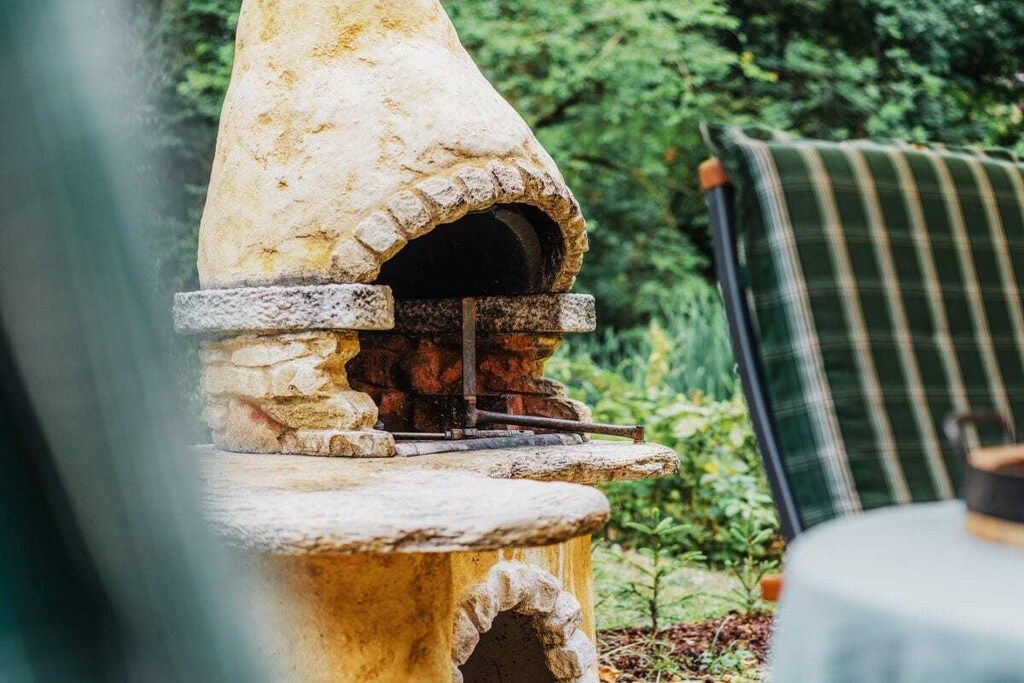 A stone-built outdoor oven with a chimney, surrounded by greenery.