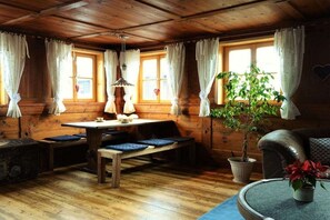 A cozy cabin interior with a wooden dining table, benches, a potted plant, and a leather sofa. - Morning Dew - Rosenhof-Allgäu (Görisried)