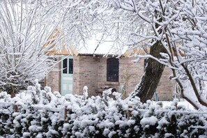 Ein Backsteinhaus mit grüner Tür, umgeben von schneebedeckten Bäumen und Sträuchern.