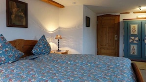 Quarto com cama, cabeceira de madeira, mesa de cabeceira com abajur, guarda-roupa de madeira e uma porta.