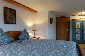 A bedroom with a bed, wooden headboard, a nightstand with a lamp, a wooden wardrobe, and a door. - Morning Dew - Rosenhof-Allgäu (Görisried)