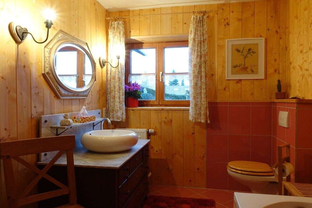 A wooden-paneled bathroom with a round mirror, a sink, a toilet, and a window with curtains.