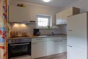 Eine Küche mit weißen Schränken, einem Herd, einem Backofen, einem Fenster und einem Kühlschrank.