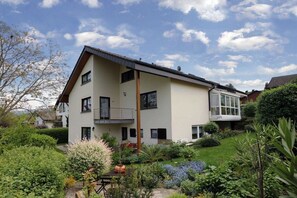 A two-story house with a balcony, surrounded by a well-maintained garden with various plants and flowers. - Holiday apartment with 2 bedrooms (Schliengen)