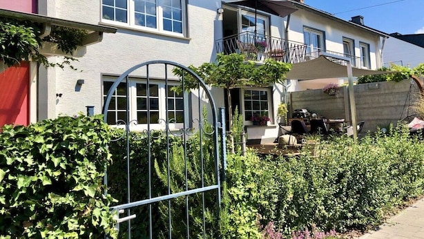 Ein zweistöckiges Haus mit einem Balkon, einem Garten mit einem Metallzaun und einer Betonmauer.
