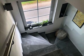 Een moderne trap met uitzicht door een raam, een klein plankje met planten en een gestructureerde vloer.
