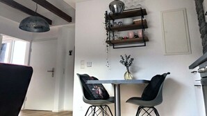 Ein Essbereich mit Tisch, zwei Stühlen, einer Pendelleuchte und einem an der Wand befestigten Regal mit Geschirr.