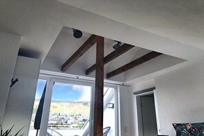 Ett rum med ett sluttande tak, synliga träbjälkar, ett stort fönster och utsikt över ett landskap.
