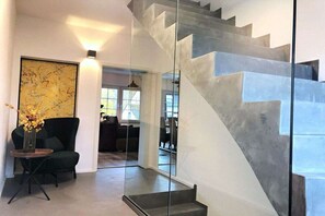 A modern interior with a staircase, a black armchair, a vase with flowers, and a large abstract painting. - Mosel-side apartments (Mehring)