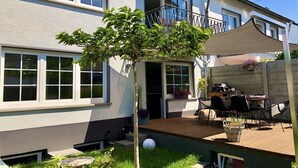 Ein zweistöckiges Haus mit einem Balkon, einer Terrasse und Gartenmöbeln sowie einem kleinen Baum.