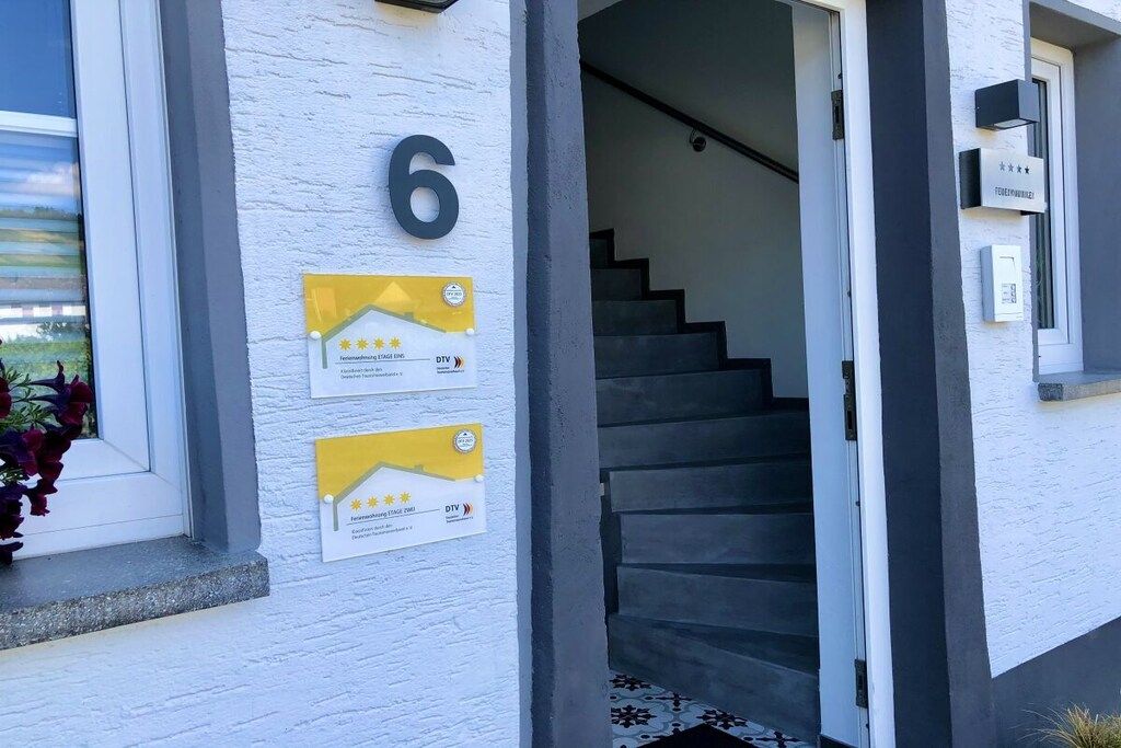 Ingresso di un edificio con un cartello con il numero '6', una scala e due targhe gialle con testo e indicazione di una valutazione a stelle.