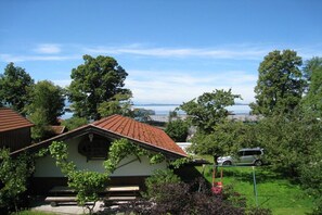 A house with a sloped roof, a garden with a swing set, and a view of the sea in the background. - Holiday apartment with 1 bedroom (Chieming)