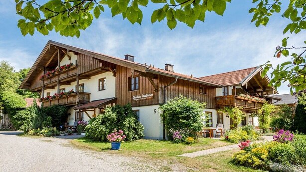 Un chalet de madera de dos pisos con balcones, rodeado de exuberante vegetación y flores.