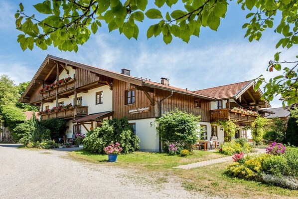 A two-story wooden chalet with balconies, surrounded by lush greenery and flowers. - Holiday apartment with 1 bedroom (Chieming)
