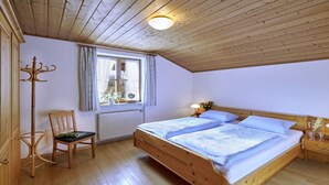 Un dormitorio con cama de madera, una silla, un ventanal con cortinas y un radiador.