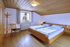 A bedroom with a wooden bed, a chair, a window with curtains, and a radiator. - Holiday apartment with 1 bedroom (Chieming)