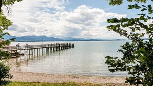 Un muelle de madera se extiende sobre un lago tranquilo con montañas al fondo.