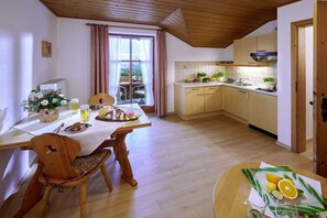 Ein Essbereich mit einem Tisch für zwei Personen, eine Küche mit Holzausstattung und ein Fenster mit Vorhängen.